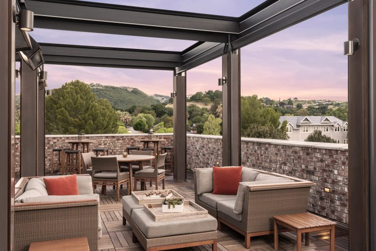 A roof top patio with comfortable seating, fire pits and a view of the sunset on the horizon.