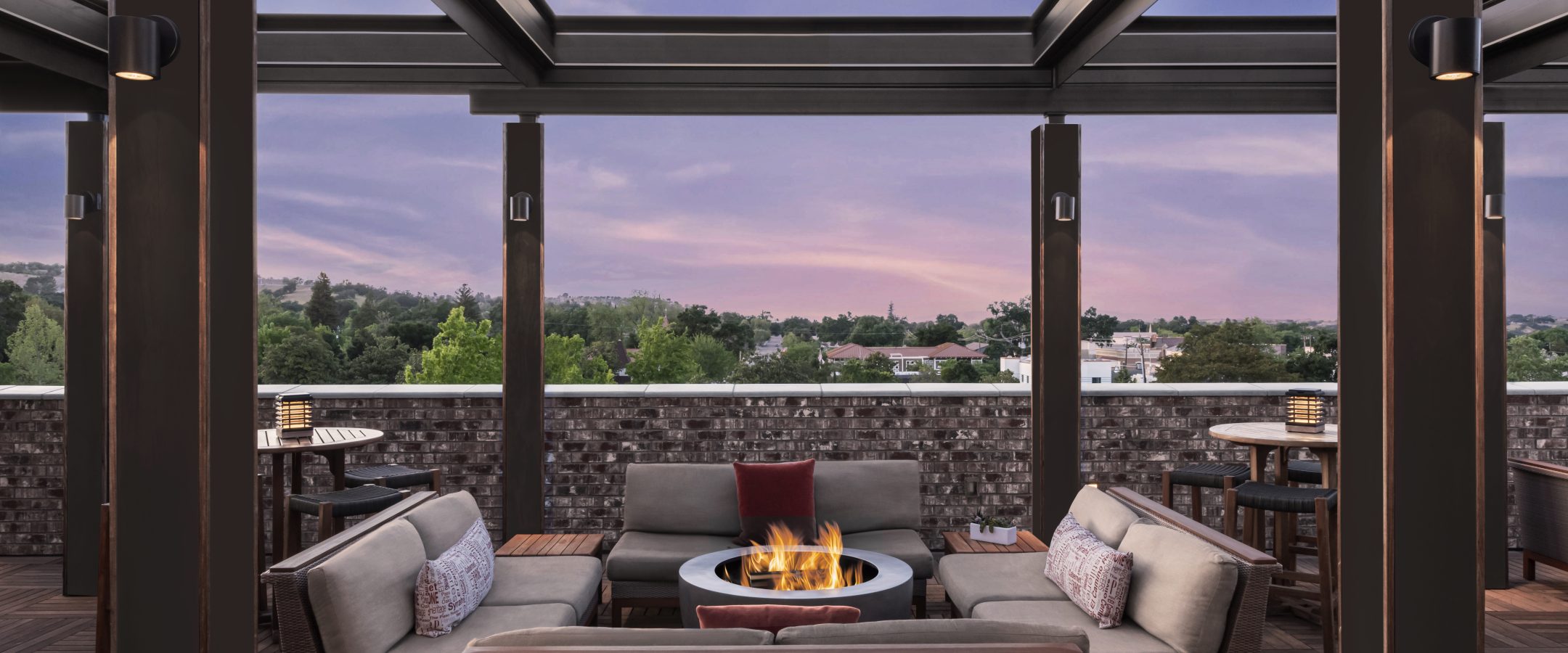 Rooftop deck at sunset. Two chairs are positioned by a firepit and the sky is purple.