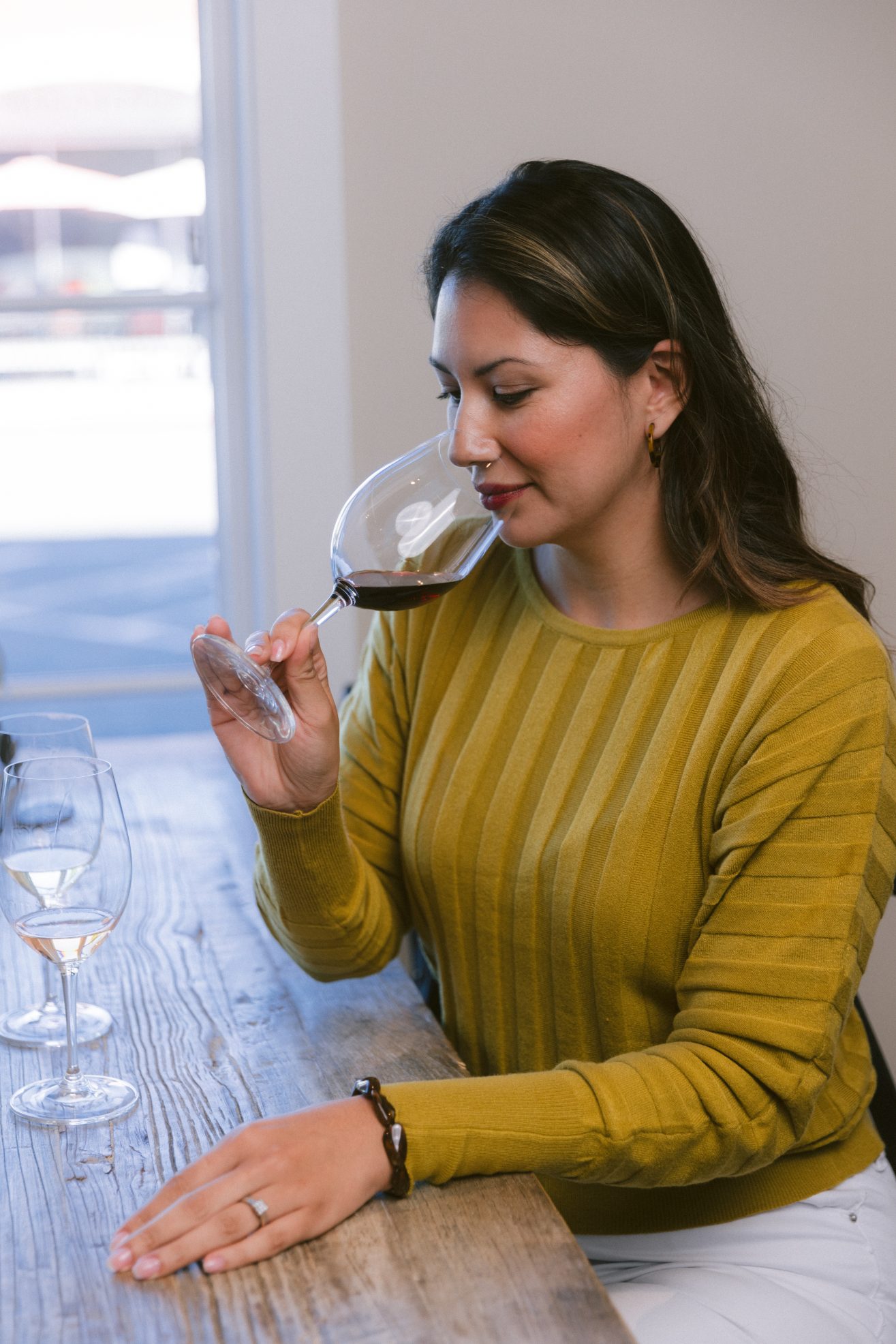 A woman in a green sweater is tasting a glass of wine.