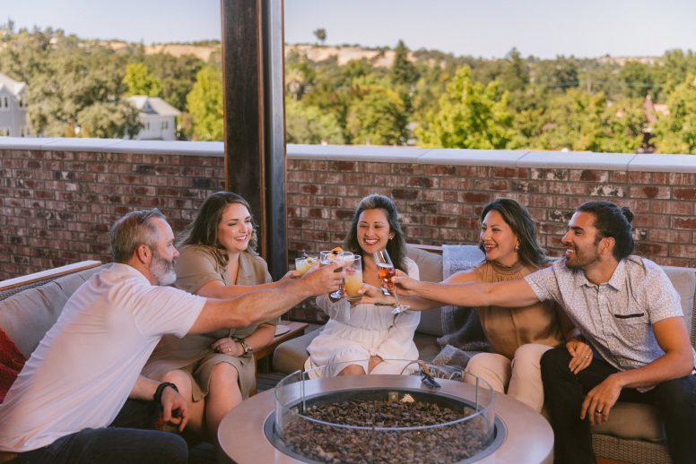 A group of friends around a fire pit on a rooftop bar toasting with cocktails.