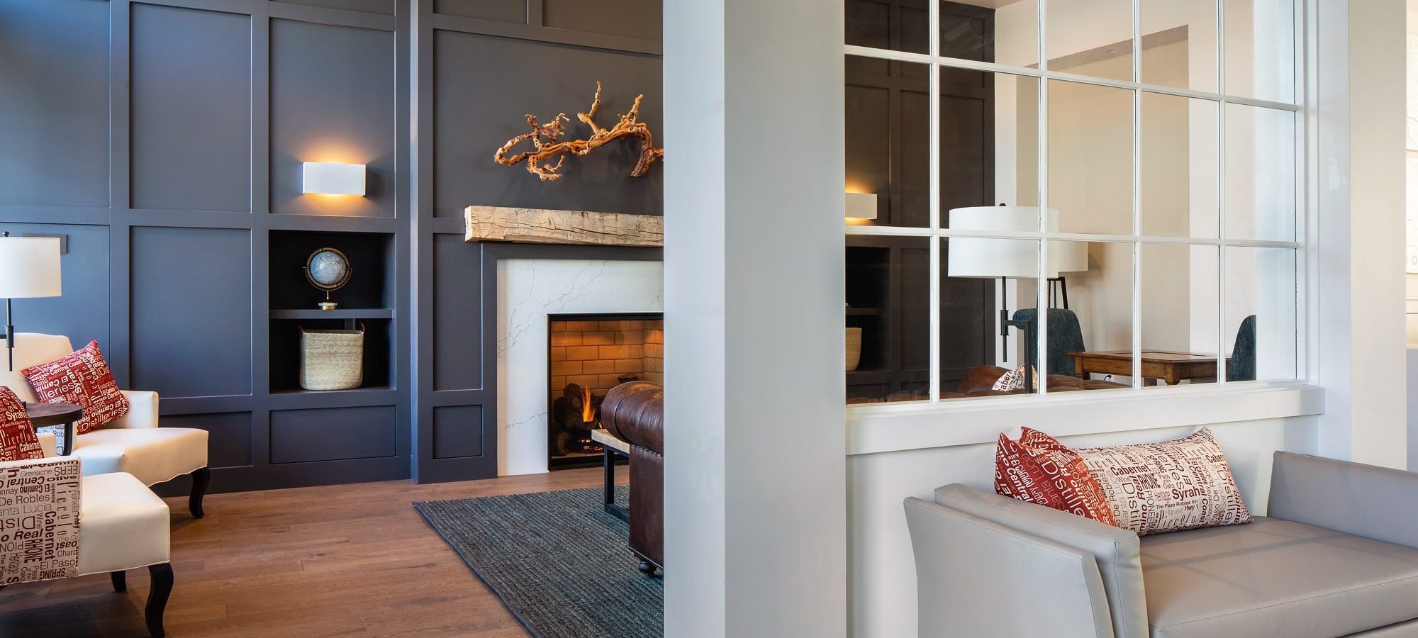 A view of a room with a fireplace and dark blue walls. There is a glass wall diving this room from a room with a sofa.