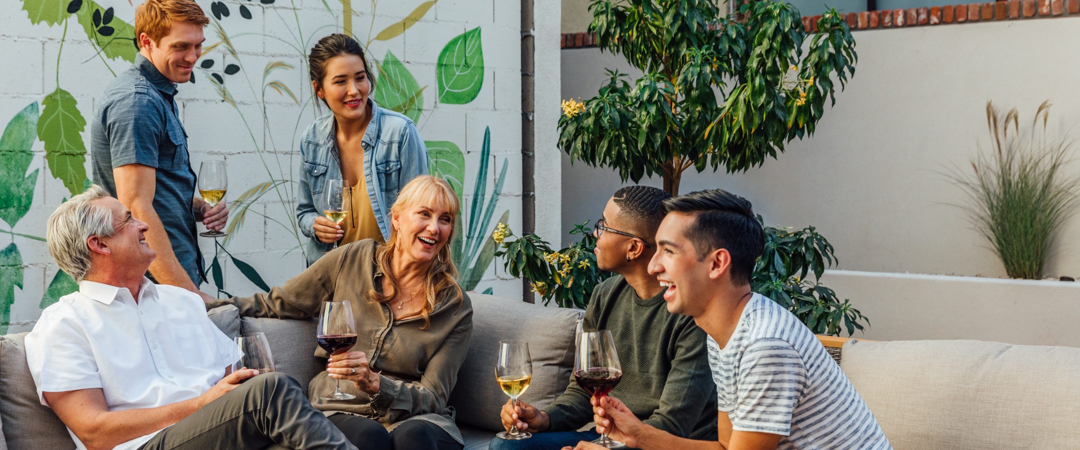 A group of friends relaxing together, some seated and some standing, holding wine glasses.