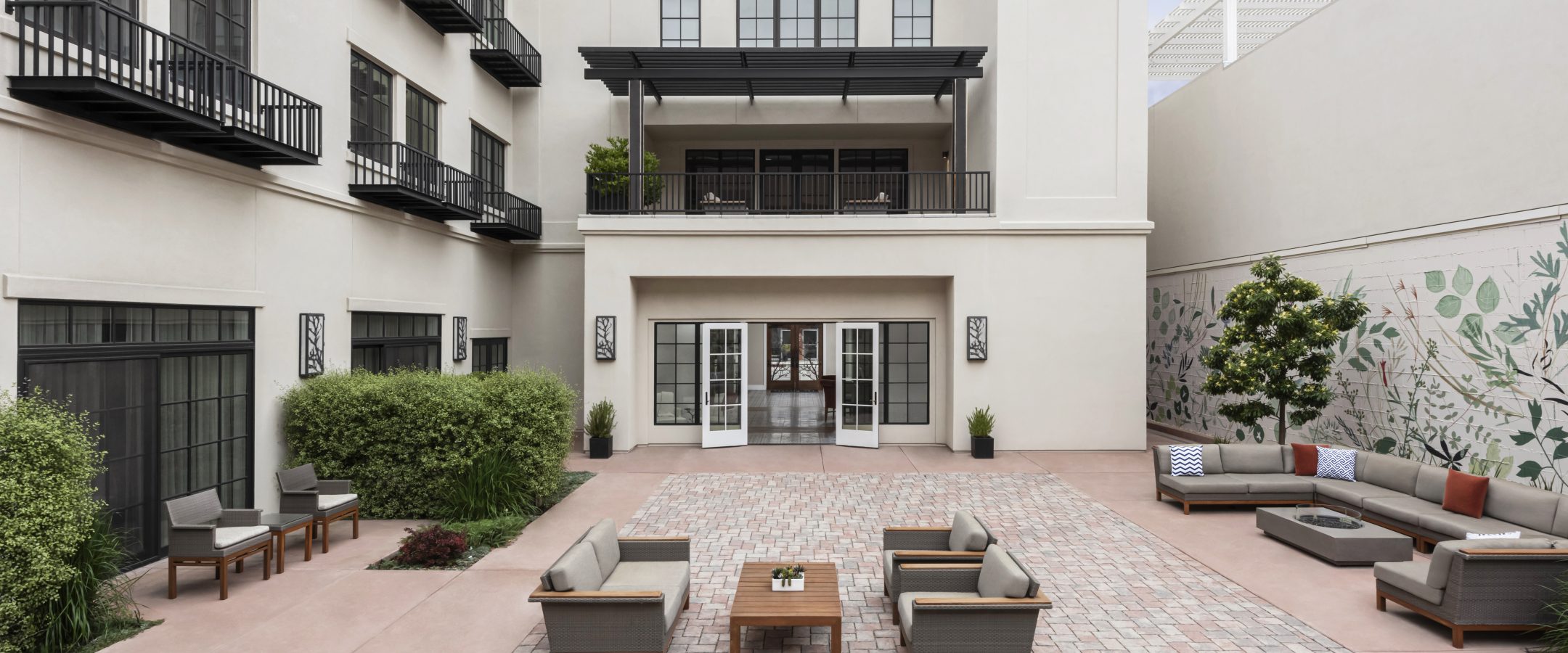 A modern outdoor courtyard with brick flooring, featuring seating arranged around a central table.