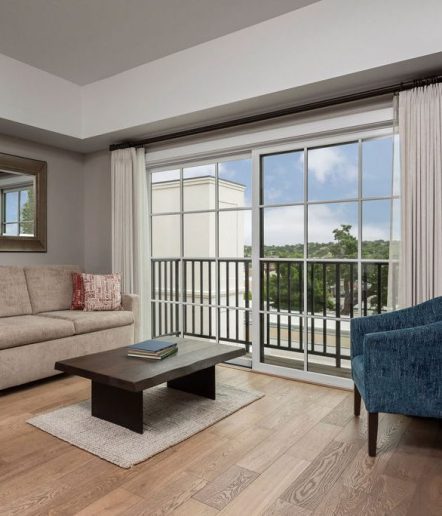 a living room with sofa, coffee table and blue chair. Sliding glass doors lead to a balcony with iron rail.