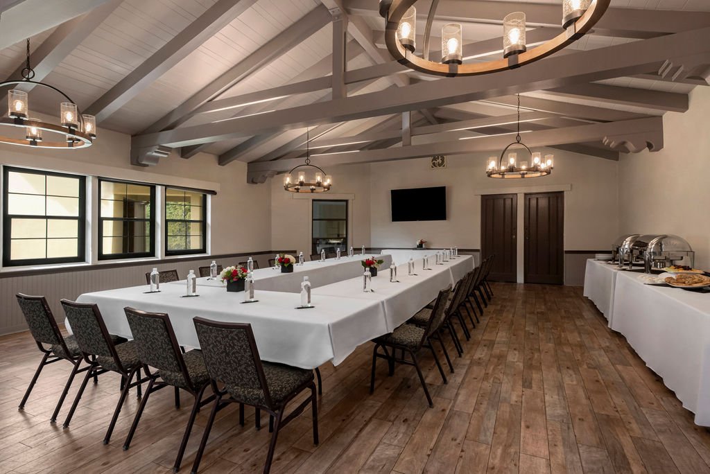 A meeting room featuring a U-shaped table draped in a white tablecloth, with bottles of water placed in front of each seat.