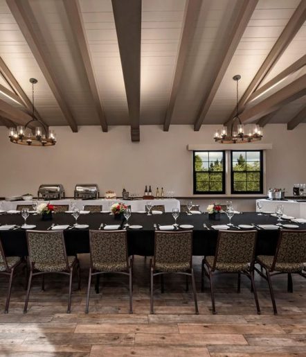 A dining table in a large room with chairs, plates, cutlery, and empty wine glasses set around the table.