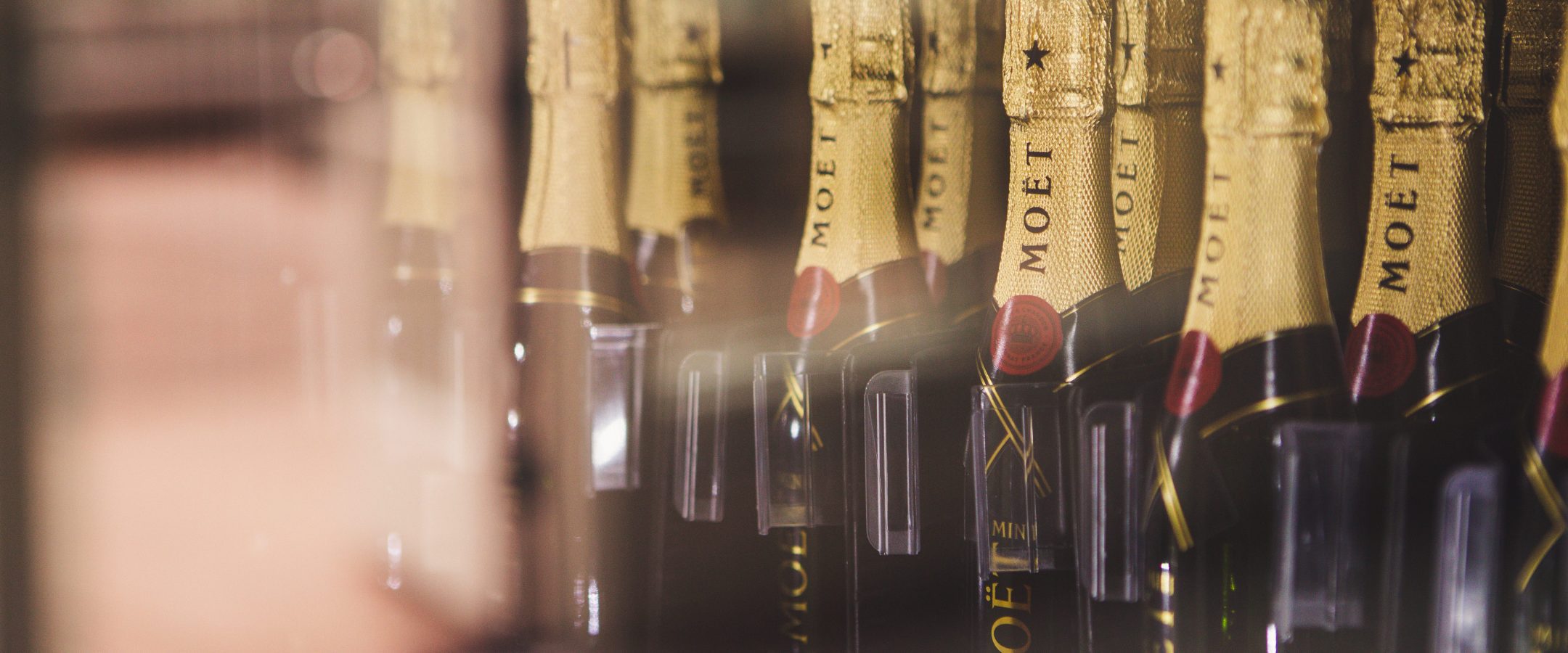 Close up shot of several mini moet champagne bottles lined up inside a vending machine.