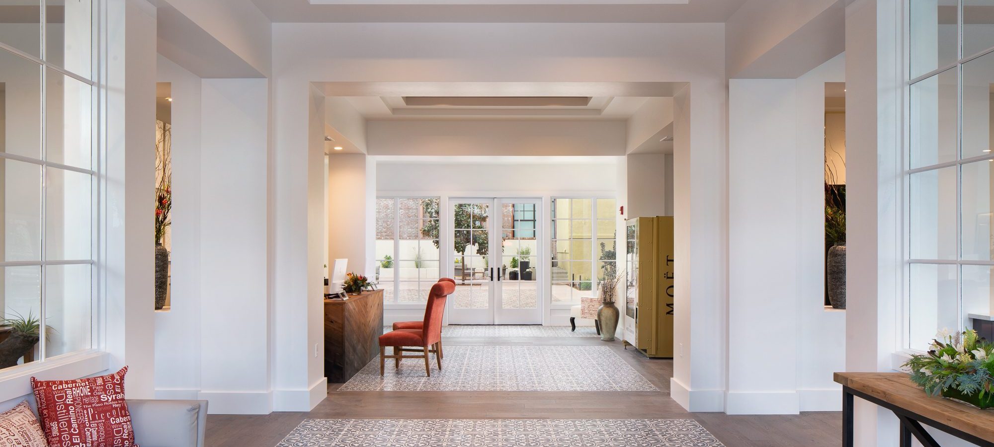 hotel lobby with reception desk, two orange chairs, a champagne vending machine, a sofa, side table and fancy patterned floors